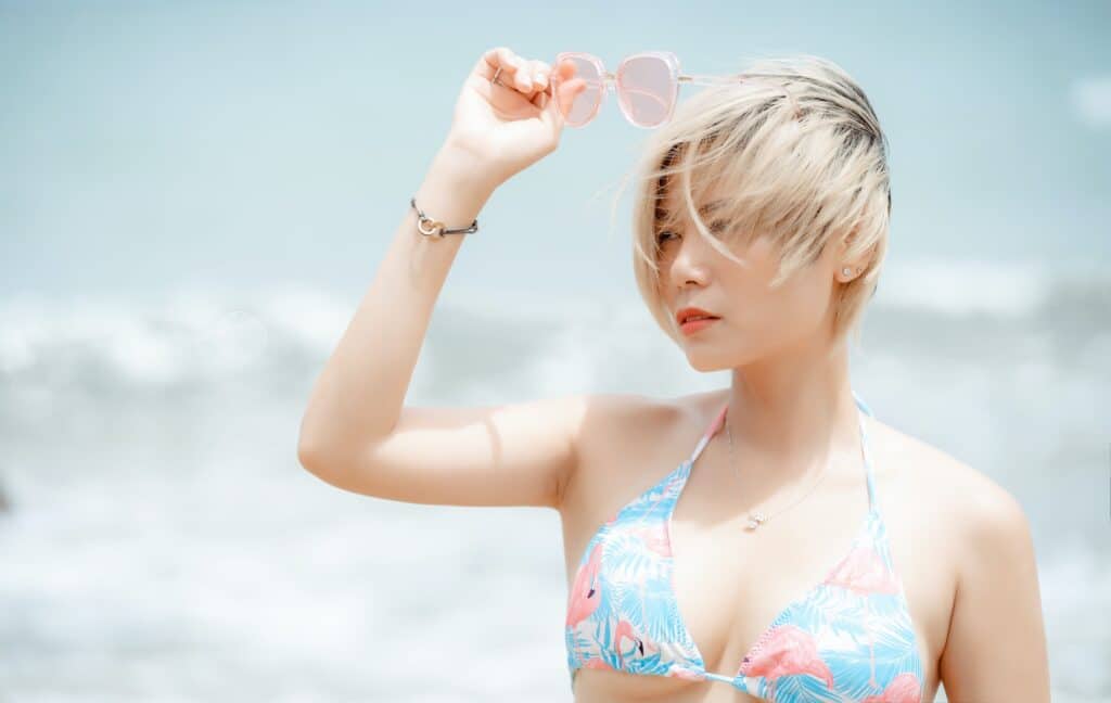 Pastel Coloured Image of a Woman Standing by a Sea and Holding Pink Sunglasses