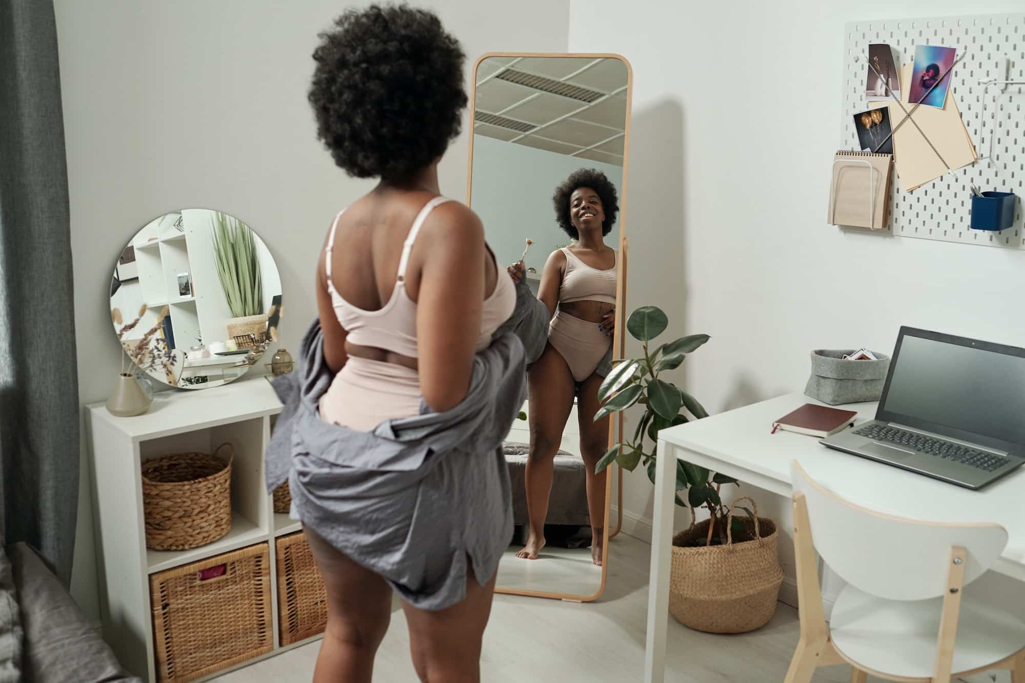 Happy young African woman in underwear looking in mirror